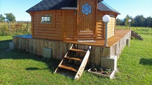 A wooden cabin with a steeply pitched roof, a front door with a decorative glass panel, and a small porch with steps leading up to it.