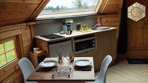A cozy cabin with a wooden interior, a dining table with chairs, a kitchen area with appliances, and a large skylight.