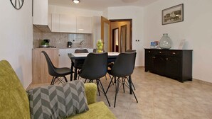 A modern kitchen with white cabinets, a dining area with a table and chairs, and a black cabinet with decorative items. - Holiday apartment with air conditioning (Štinjan)