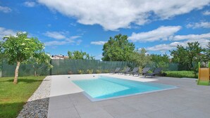 A swimming pool with a tiled deck, surrounded by a low fence, and trees in the background. - Holiday apartment with air conditioning (Štinjan)