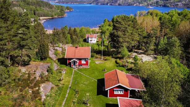 A red-roofed cabin with a small porch, surrounded by lush greenery and a large body of water in the background. - Cozy home in Strömstad with WiFi (Strömstad)