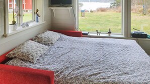 A bedroom with a bed, a red chair, a window with a view of a lake, and a dresser with a TV. - Cozy home in Strömstad with WiFi (Strömstad)