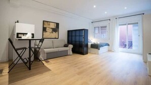 A spacious living area with a sofa, a small table, and a cabinet. There is a balcony with a view. - Barcelona - Loft Parc Güell (Barcelona)