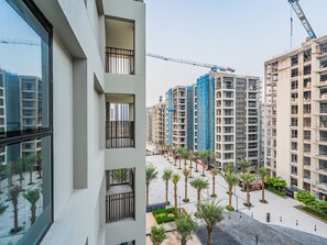 A high-rise residential building with multiple balconies, a construction crane in the background, and a landscaped courtyard with palm trees. - Creek Beachfront Heaven 1BR Luxe Harbor (Dubai)