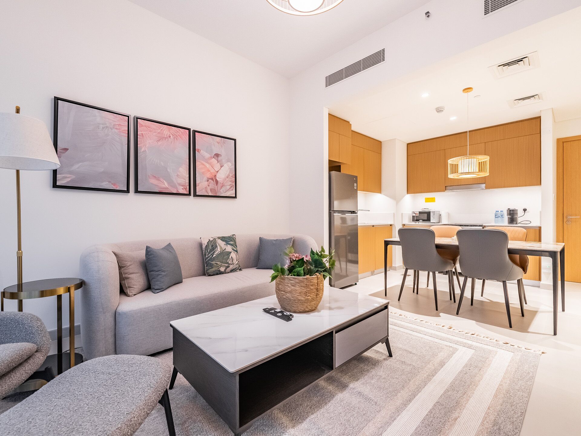 A modern living room with a sofa, coffee table, and a dining area with chairs and a kitchen in the background.