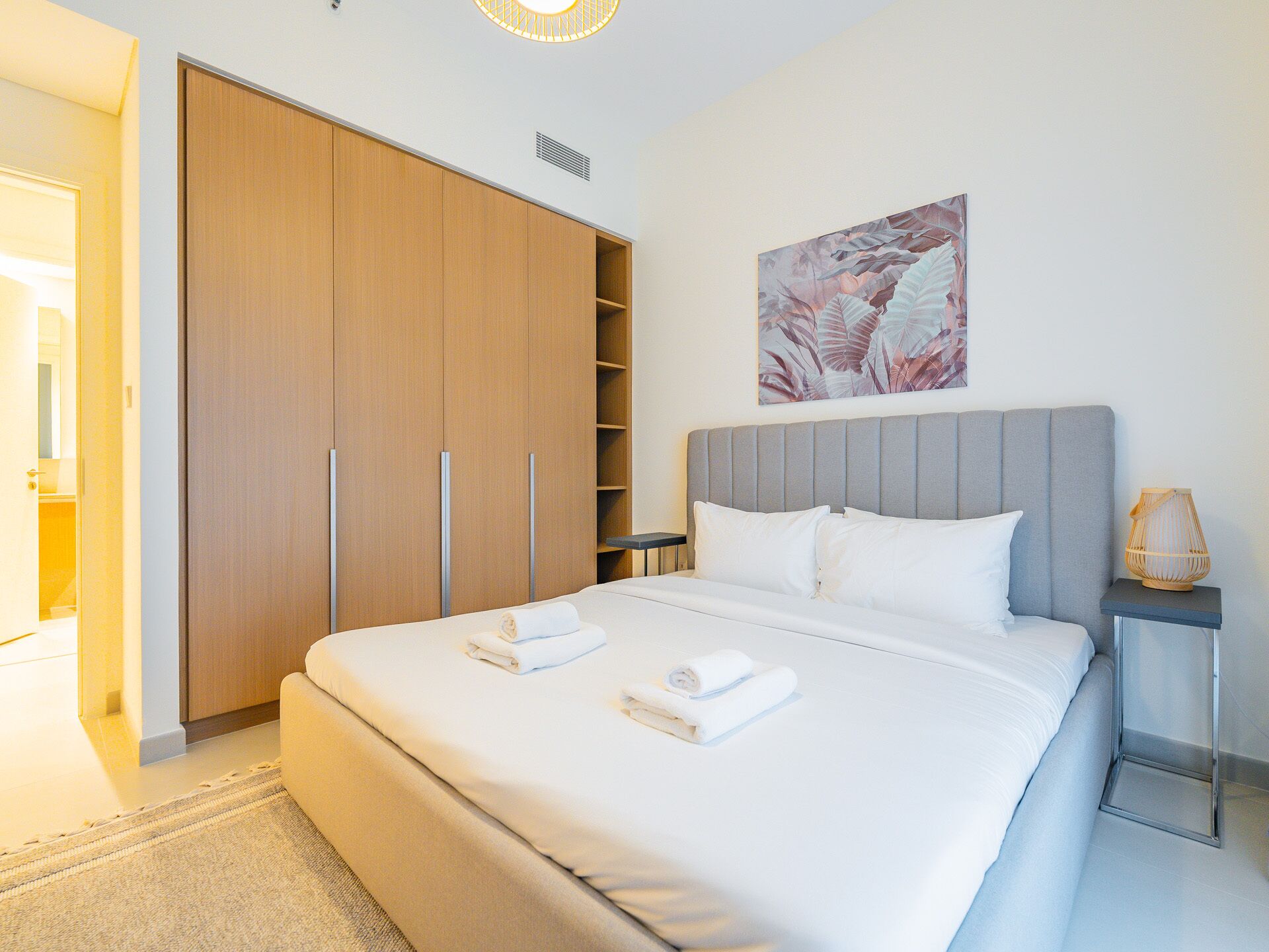 A modern bedroom with a large bed, a grey headboard, and a wooden wardrobe.