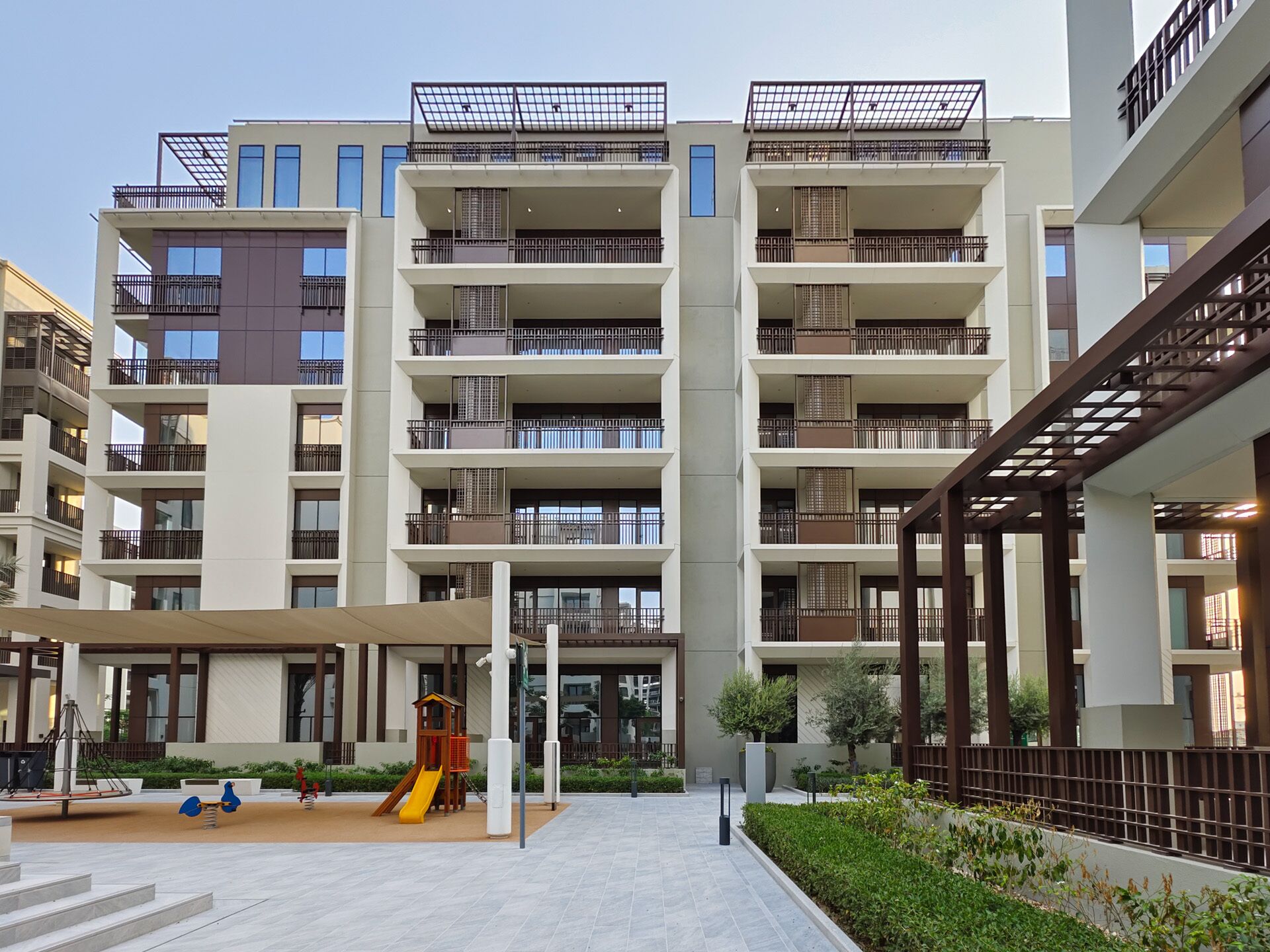 A multi-story residential building with balconies, a playground, and a covered outdoor area.