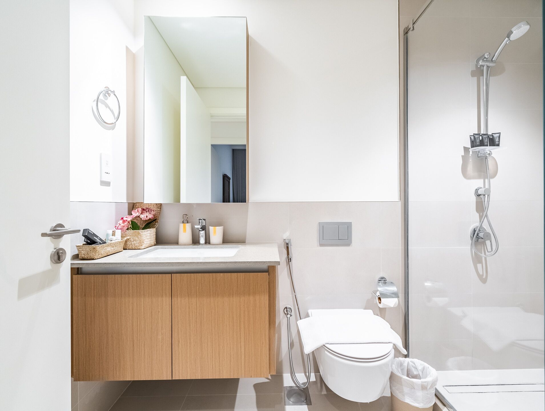 A modern bathroom with a wooden vanity, a large mirror, a shower with a handheld showerhead, and a toilet.