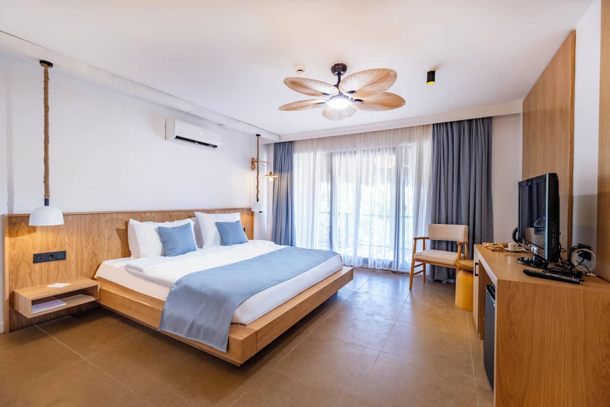 Een moderne hotelkamer met een houten bed, een bureau met een televisie en een plafondventilator.