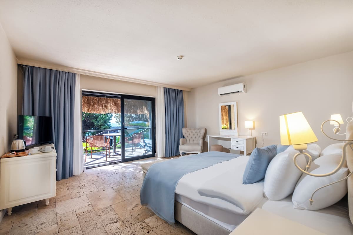 Een hotelkamer met een bed, een bureau, een stoel, een televisie en een balkon met buitenmeubilair.
