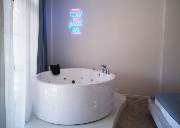Un baño moderno con una bañera blanca grande, un letrero de neón en la pared y una cama con cubrecama azul.
