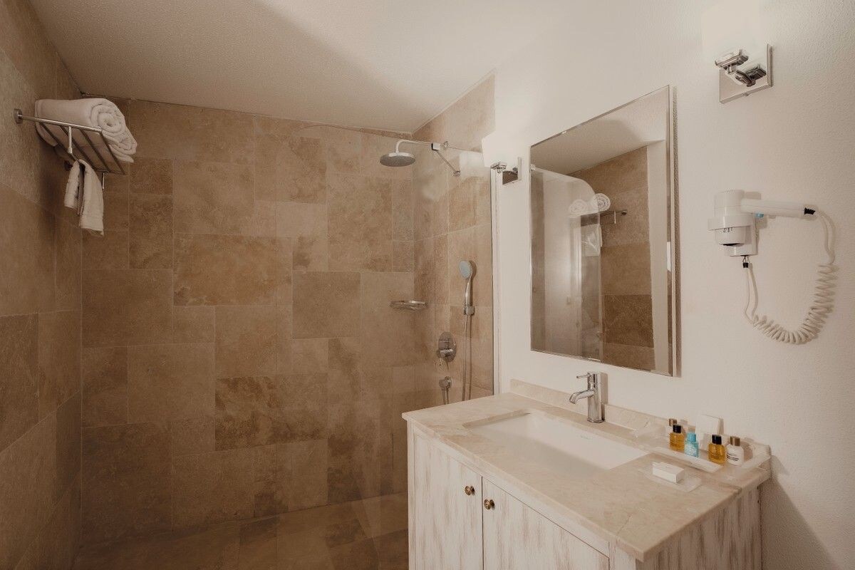 Un baño con ducha, lavabo, espejo y secador de pelo en la pared.