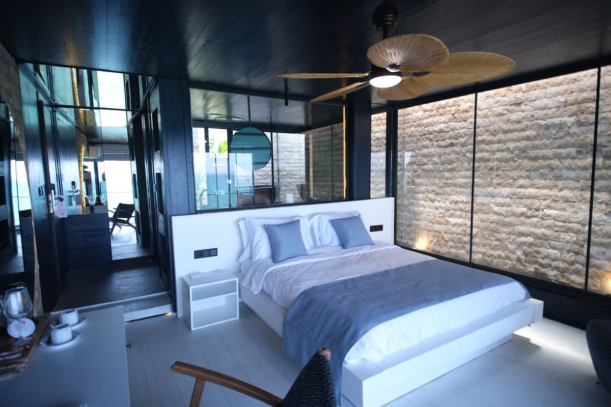 Een moderne slaapkamer met een groot bed, een plafondventilator en een stenen muur.