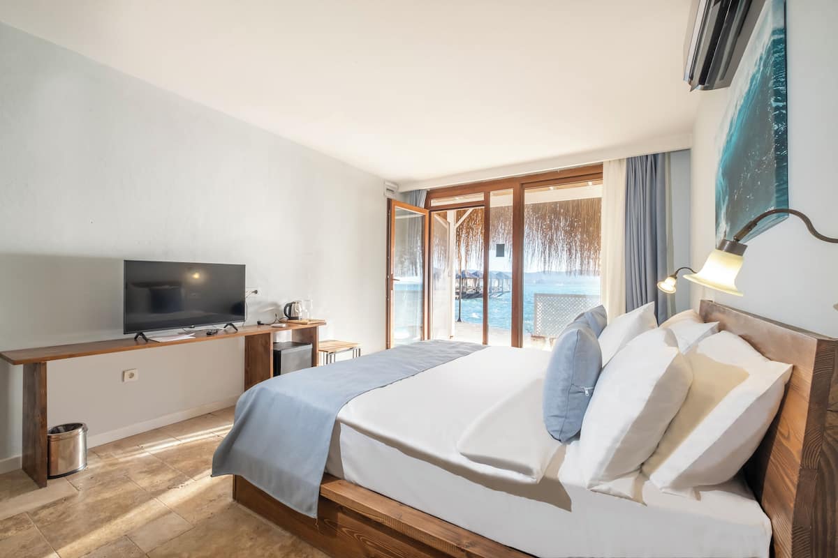 Een hotelkamer met een bed, een televisie, een bureau en uitzicht op zee.