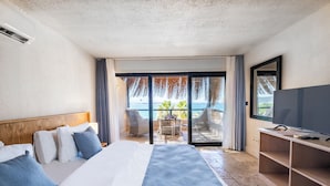 Une chambre d’hôtel avec un grand lit, une télévision et une vue sur l’océan, accessible par une porte-fenêtre coulissante.