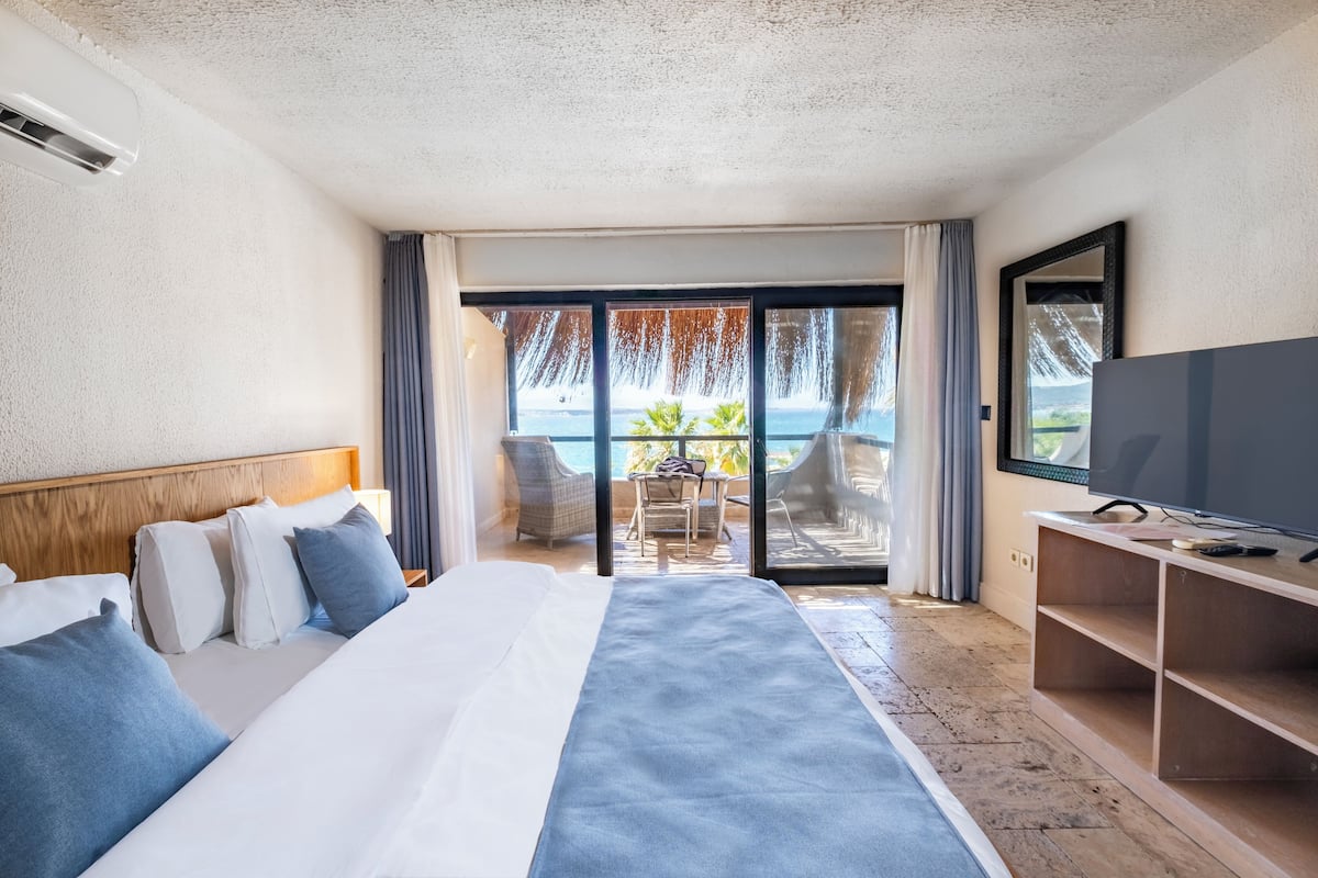 Een hotelkamer met een groot bed, een televisie en uitzicht op de oceaan door een schuifdeur.