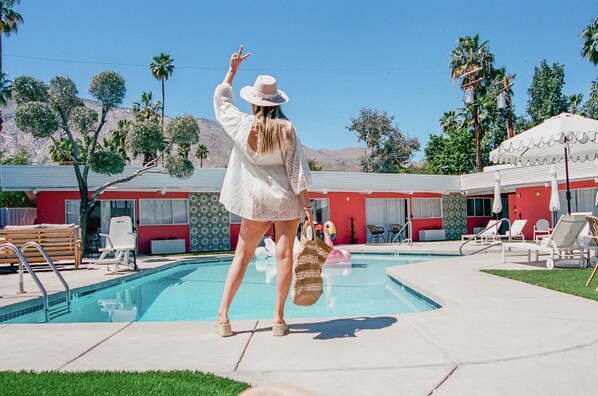 A pool area with lounge chairs, a pool, and a building with red and white exterior walls. - Marilyn Suite · Private Yard (Palm Springs)