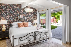 Een slaapkamer met bloemenbehang, een bed met witte lakens, twee nachtlampjes en een grote spiegel.