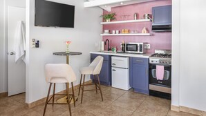 A compact kitchen with a flat-screen TV, a microwave, a stove, and a sink. There are two bar stools and a small table with a vase of flowers. - The Sofia Suite · Adults-Only Palm Springs Pool (Palm Springs)