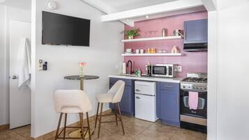 Cozinha compacta com televisão de tela plana, micro-ondas, fogão e pia. Há dois bancos altos e uma pequena mesa com um vaso de flores.