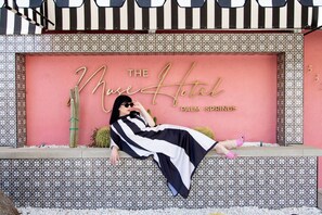 En kvinde slapper af foran en lyserød væg med teksten "The Muse Hotel Palm Springs".