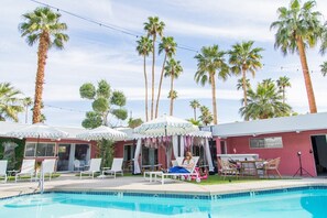 A poolside area with lounge chairs, a covered seating area, and palm trees.