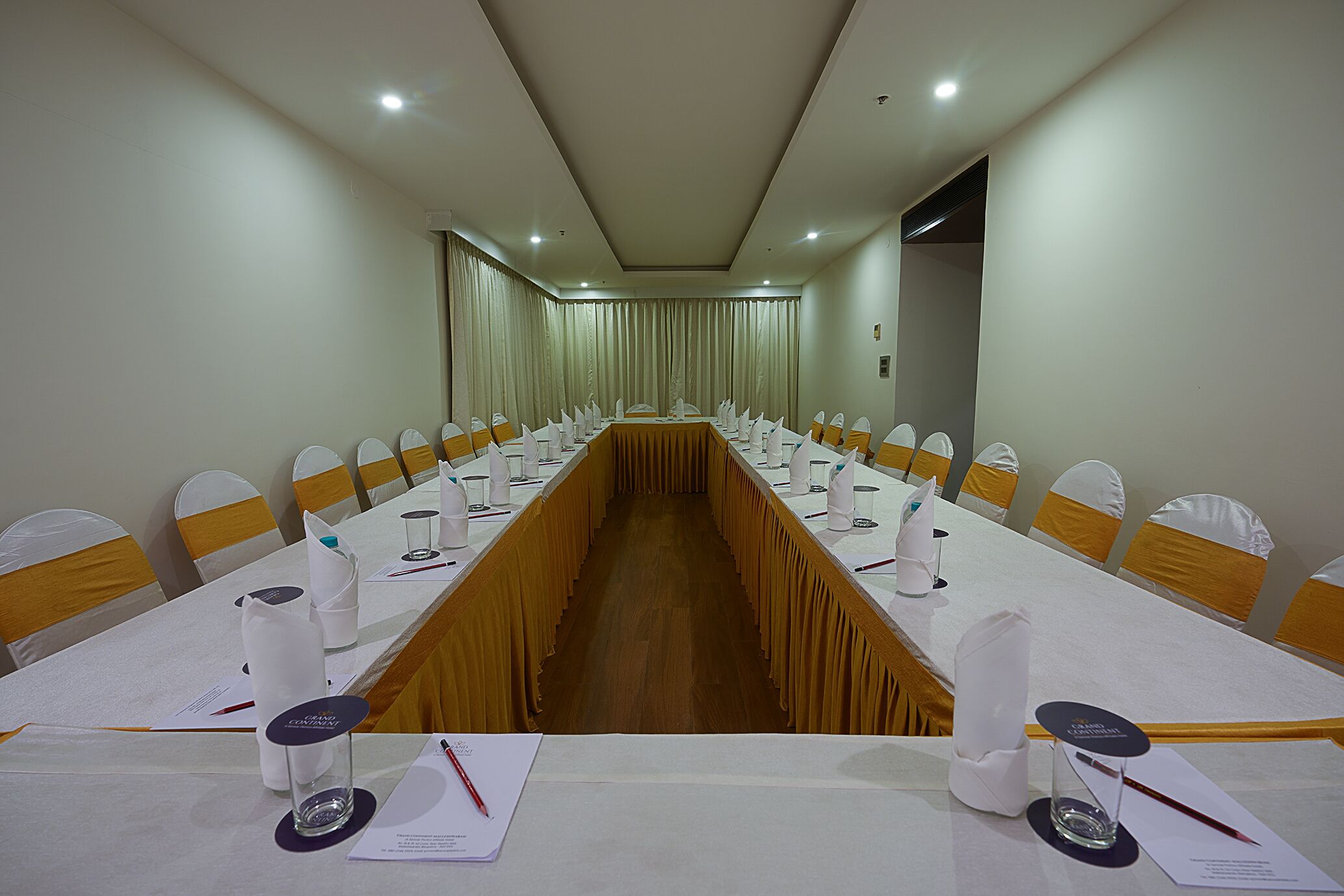 A conference room with a long table, white chairs, and a wooden floor.