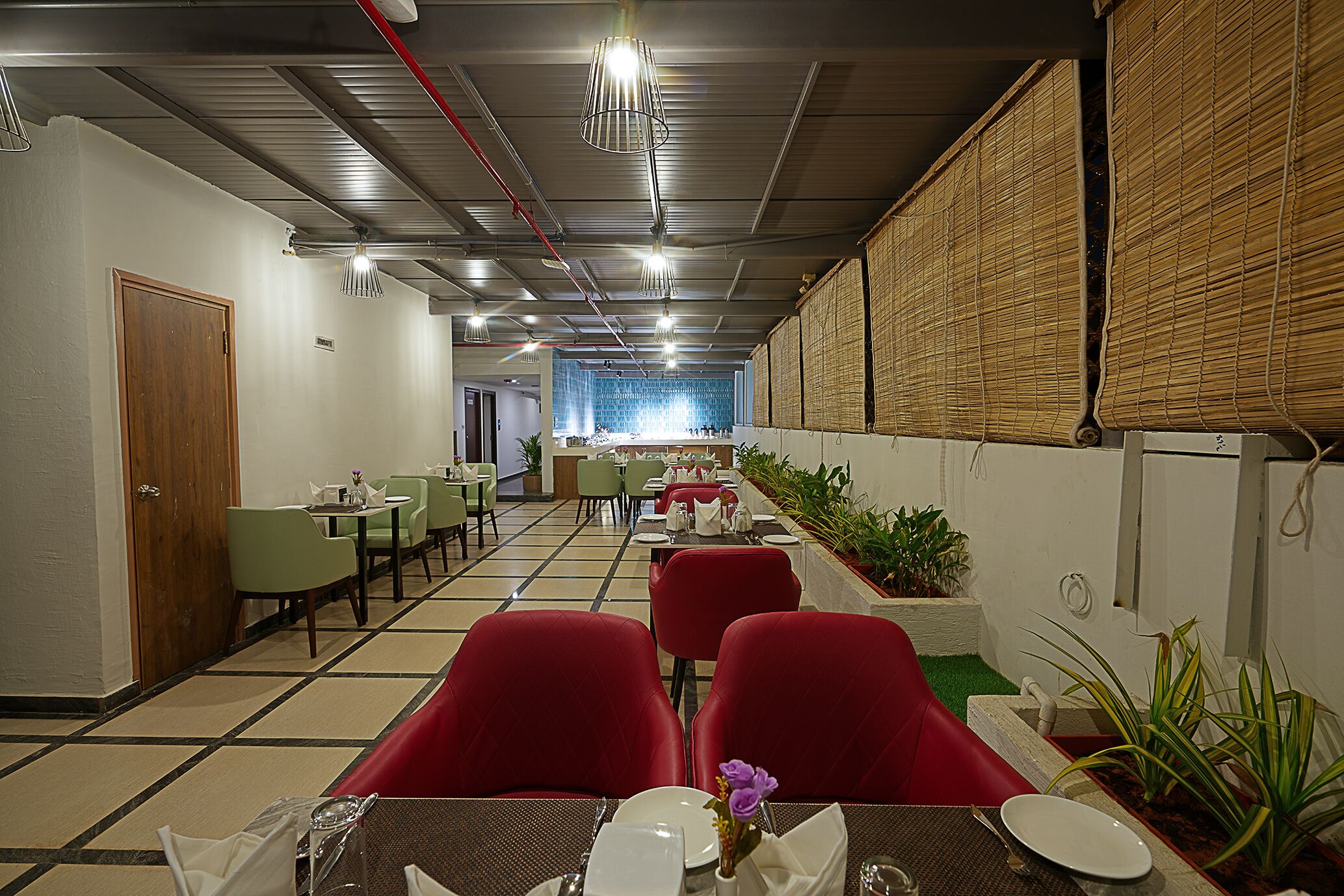 A restaurant with red chairs, tables set with white plates and glasses, and a tiled floor.