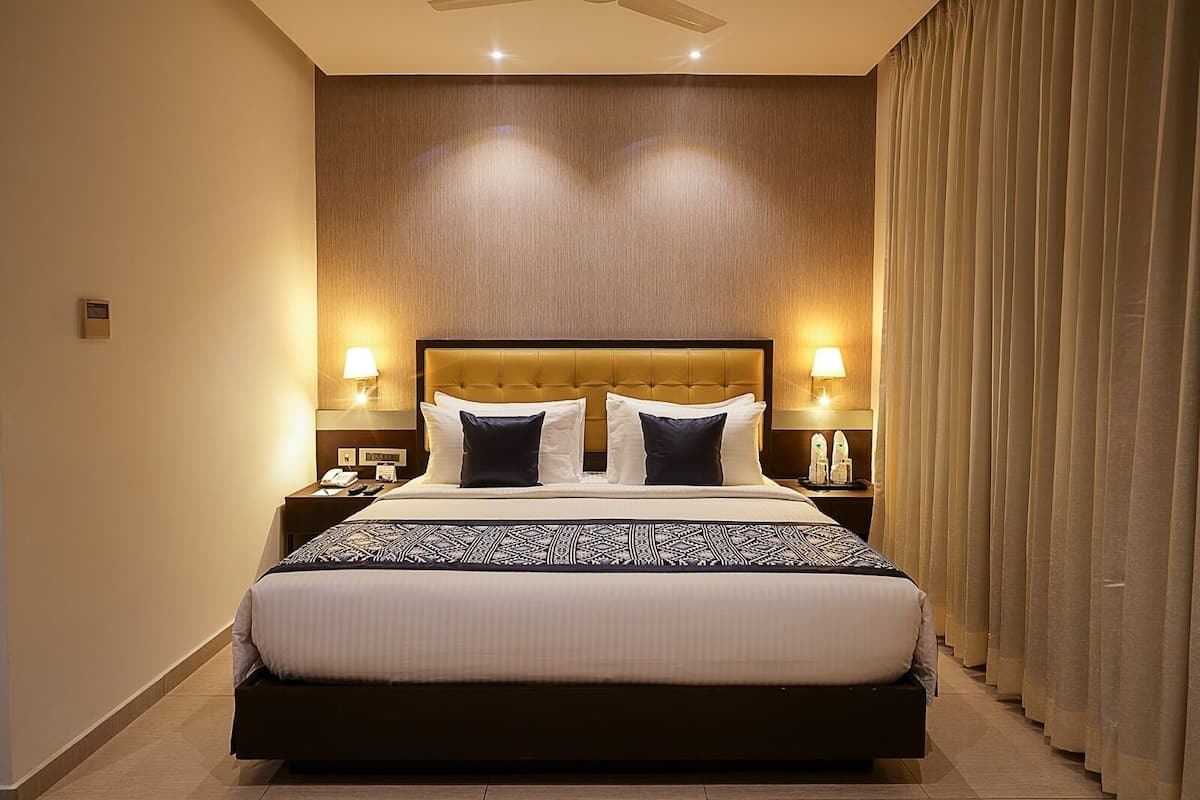 Habitación de hotel con una cama grande, dos mesitas de noche con lámparas, un ventilador de techo y una ventana con cortinas.