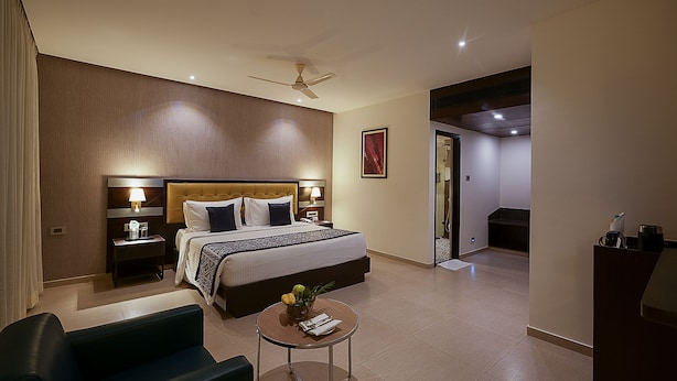 A hotel room with a large bed, bedside tables with lamps, a small round table with a plant, and a ceiling fan. - Grand Continent Malleshwaram A Sarovar Portico Affiliate Hotel (Bengaluru)