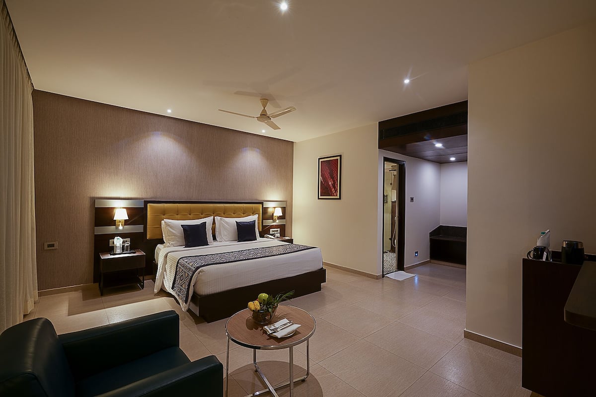 Habitación de hotel con una cama grande, mesitas de noche con lámparas, una pequeña mesa redonda con una planta y un ventilador de techo.