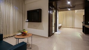 A modern hotel room with a flat-screen TV mounted on the wall, a small round table with a fruit bowl, a sofa, and a bed in the background. - Grand Continent Malleshwaram A Sarovar Portico Affiliate Hotel (Bengaluru)