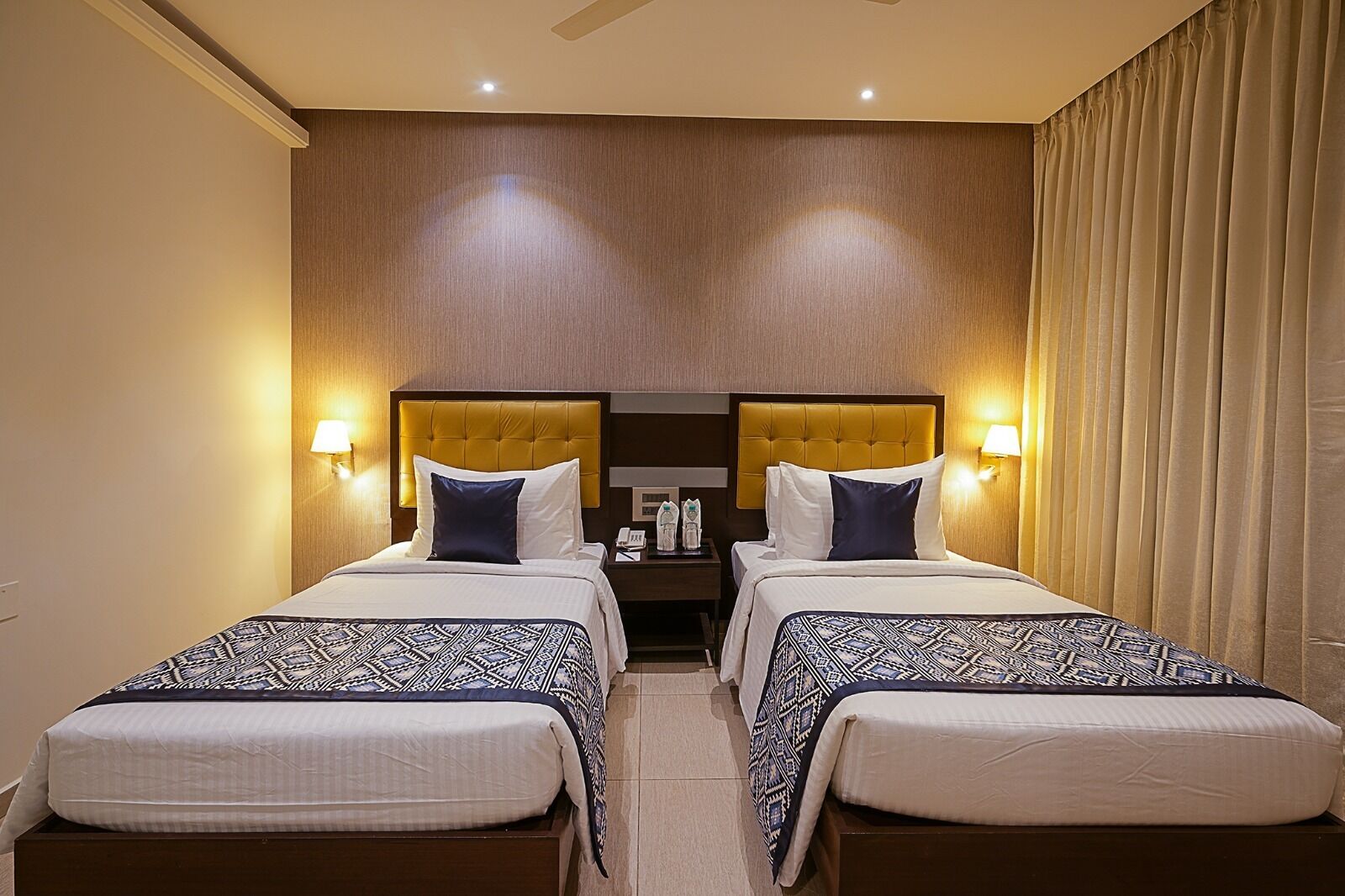 A hotel room with two beds, each with a headboard, bedside tables, and lamps.