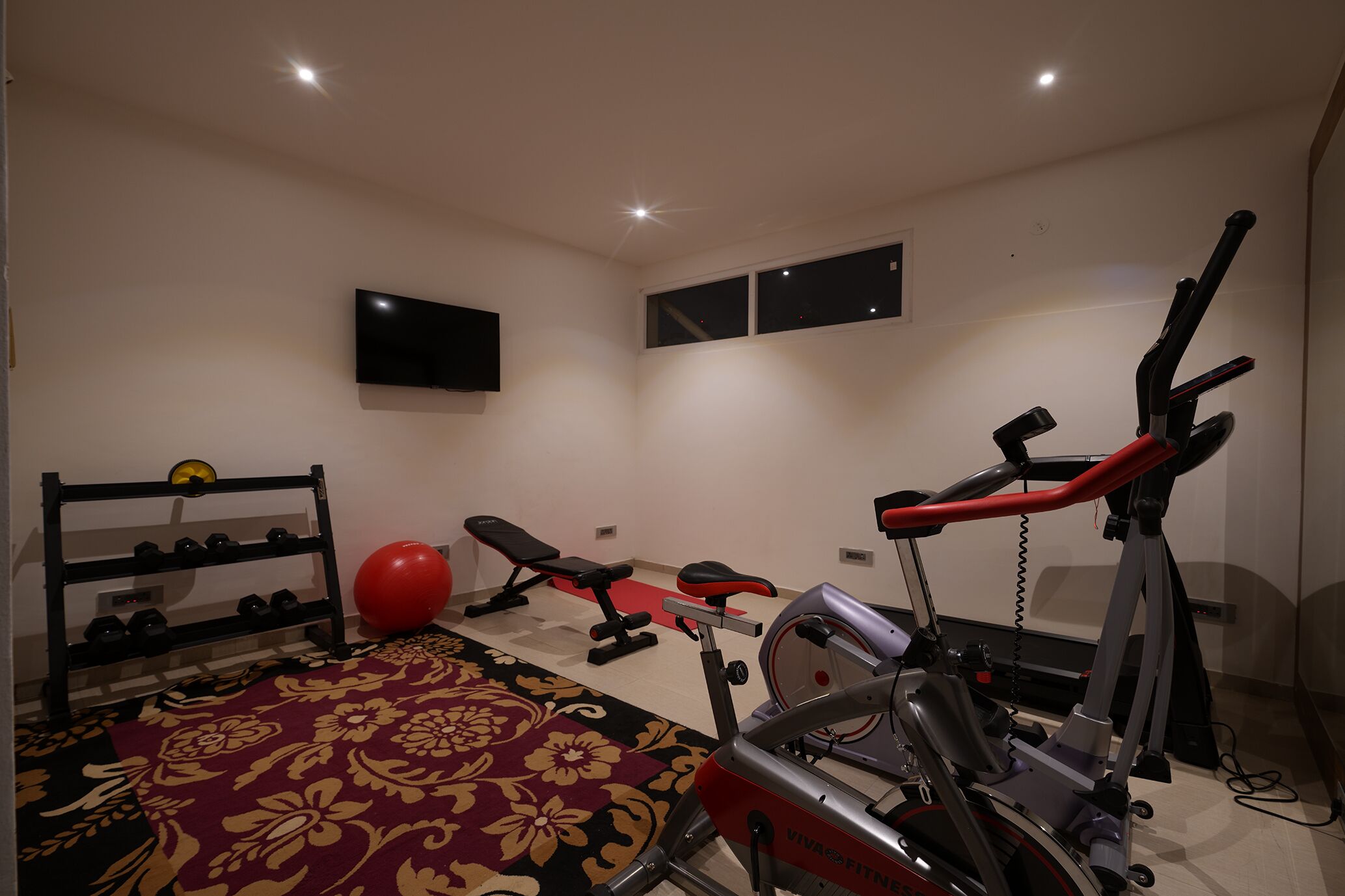 Uma academia em casa com esteira, bicicleta ergométrica, banco e suporte para halteres.