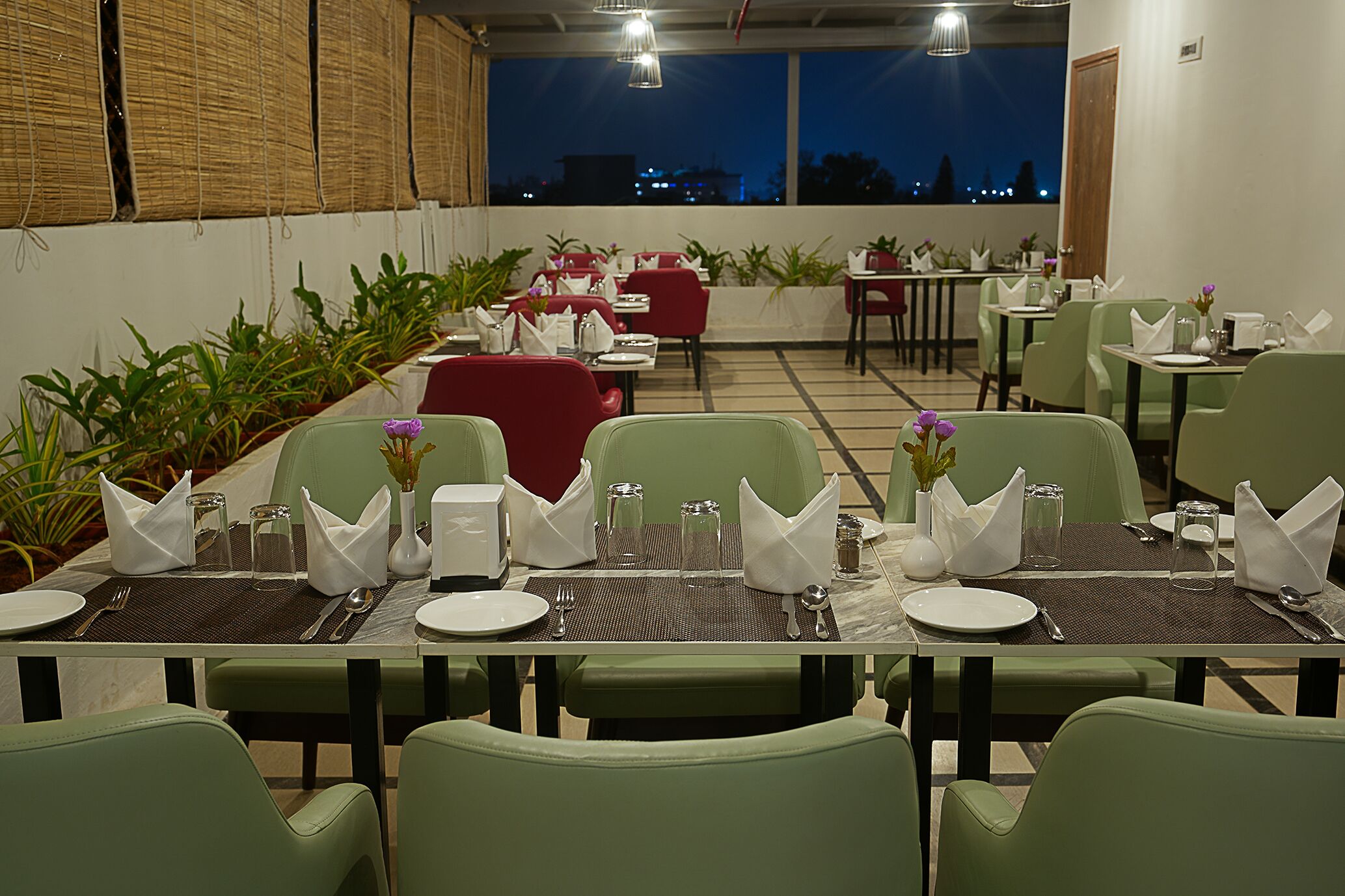 A restaurant with tables set for dining, chairs, and a view of the city at dusk.