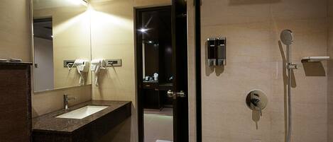 A hotel bathroom with a sink, mirror, hairdryer, and shower.
