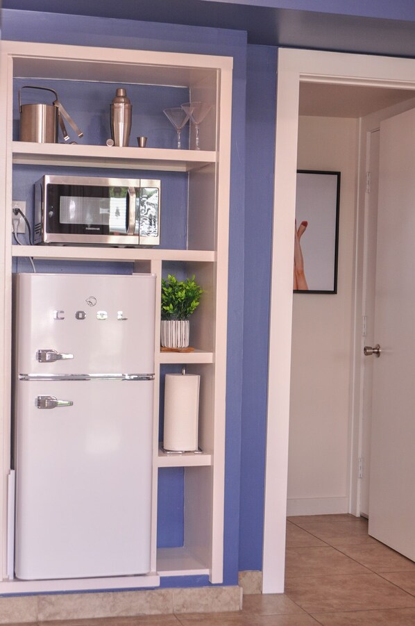 A kitchen with a white refrigerator, a microwave, and a shelf with kitchenware.