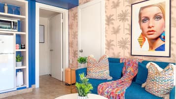 A living room with a blue sofa, colorful pillows, a white coffee table, and a framed picture on the wall.
