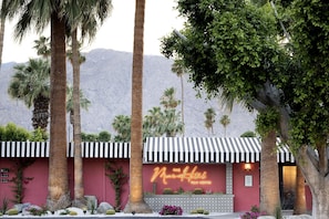 A hotel with a neon sign, palm trees, and a mountain in the background.