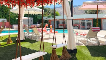 A poolside area with lounge chairs, a swing, and a view of a mountain range.