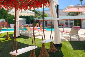 Un área junto a la piscina con sillones de descanso, una hamaca y vistas a una cadena montañosa.