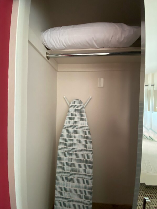 Ein kleines Zimmer mit einem Bett, einem an der Wand befestigten Bügelbrett und einem kleinen Fenster.