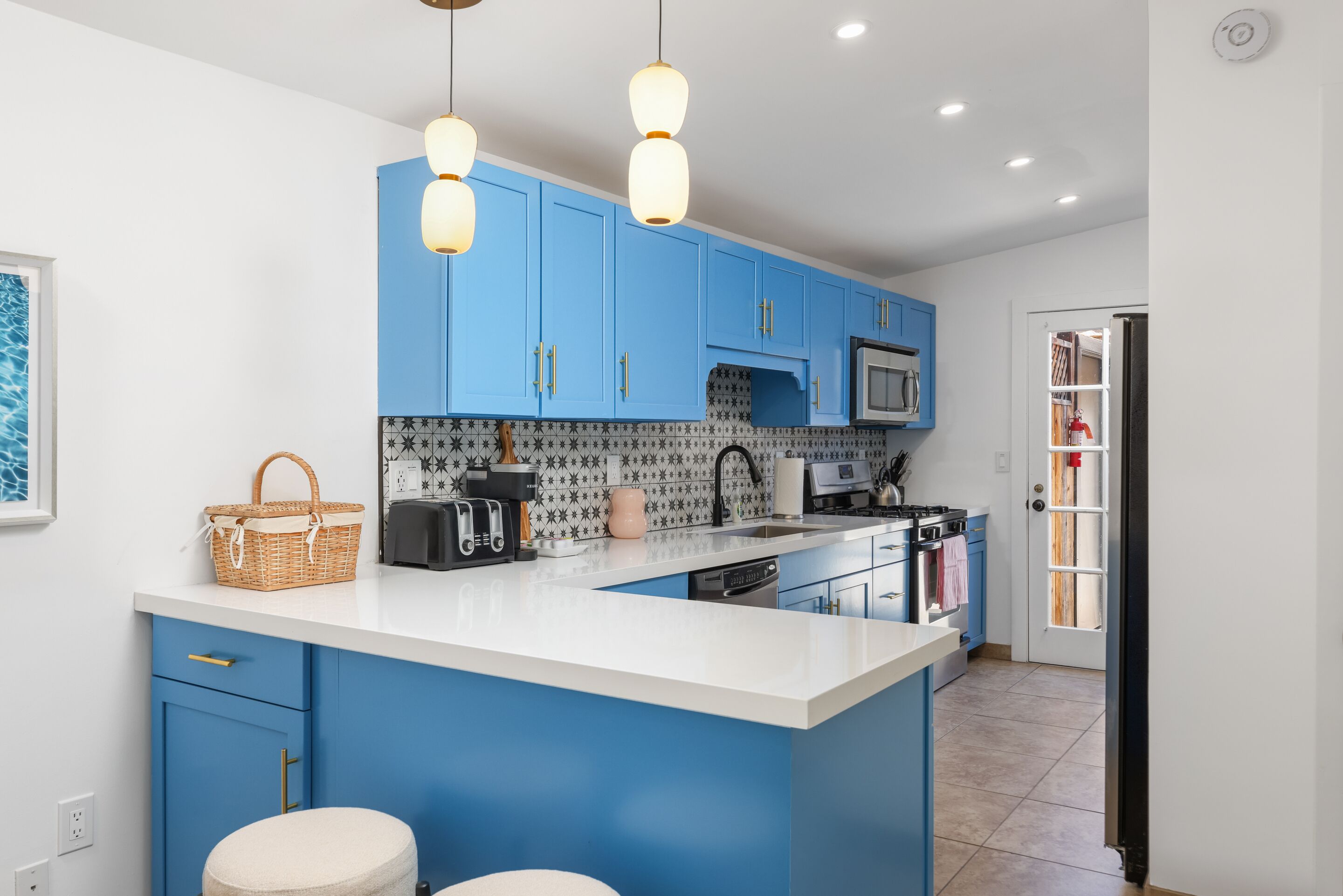 Een moderne keuken met blauwe kastjes, een wit aanrechtblad en hangende lampen.