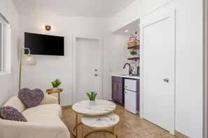 A compact living space with a sofa, two round tables, a TV, a kitchen area, and a door. - The Kate Suite · Two Queens · Palm Springs Pool (Palm Springs)