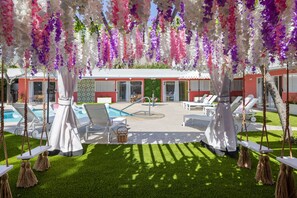 A poolside area with white lounge chairs, a small pool, and hanging floral decorations. - The Kate Suite · Two Queens · Palm Springs Pool (Palm Springs)