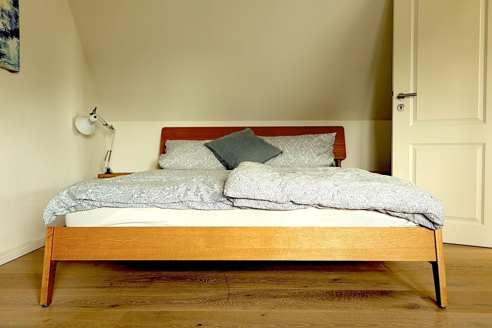A single bed with a wooden frame, a bedside lamp, and patterned bedding.