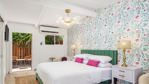 A bedroom with a green bed, white bedding, and floral wallpaper.
