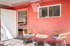 A room with a pink wall, a bed with floral wallpaper, and two wicker chairs with cushions. - Brigitte Suite · Adults-Only PS Boutique· Dog Yard (Palm Springs)