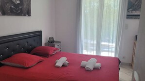 Un dormitorio con cama, ropa de cama roja, una mesita de noche, una lámpara y un cuadro en la pared.