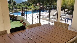 Una mesa de madera y sillas de mimbre en un balcón con vistas a una piscina y un área ajardinada.